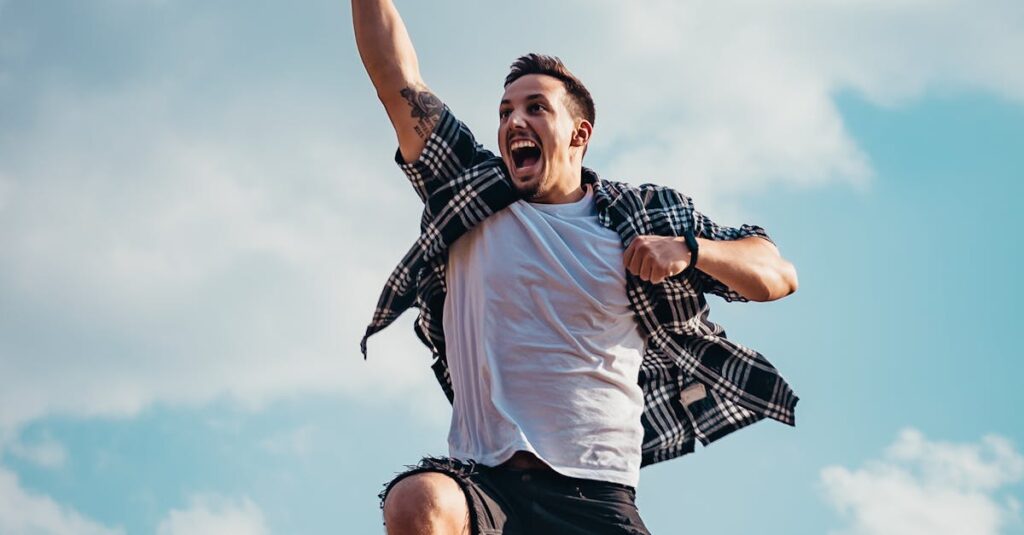 A joyful young man jumps midair with clouds and blue sky in the background, exuding energy and freedom.